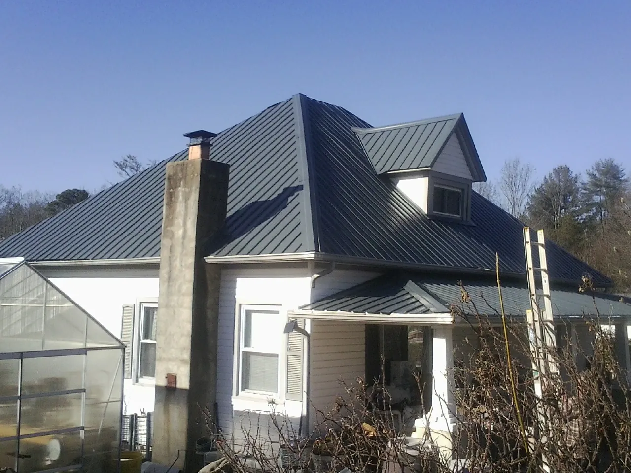 Dark blue standing seam metal roof on a white farmhouse with dormer — Slate & Tile Roof Repair by Roofing Brothers in Newborn