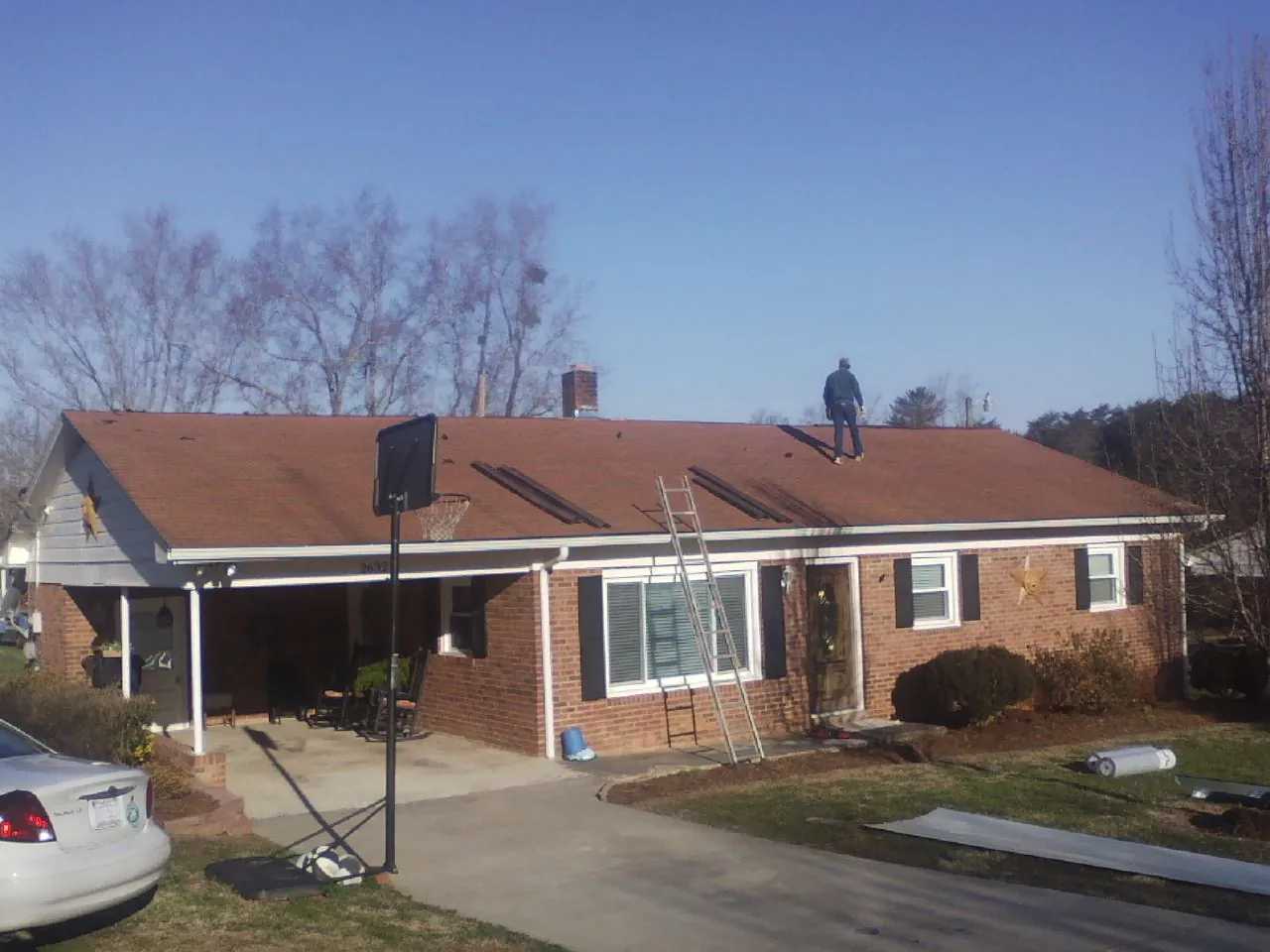 Roofer stripping a shingle roof on a brick ranch before metal panels in Newborn