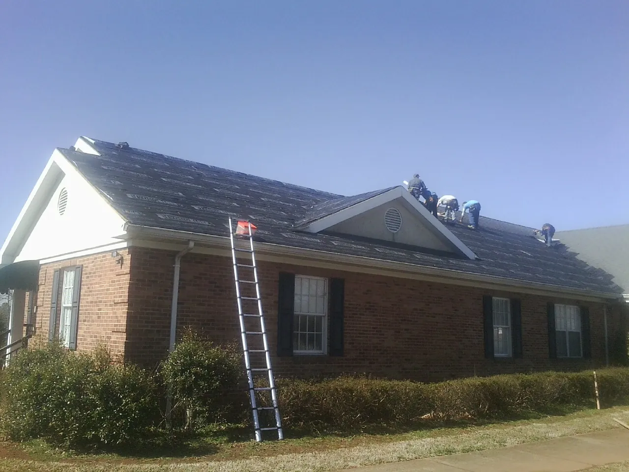 Crew tearing shingles off a brick ranch roof with a ladder set — Emergency Roof Repair work by our crew in Newborn