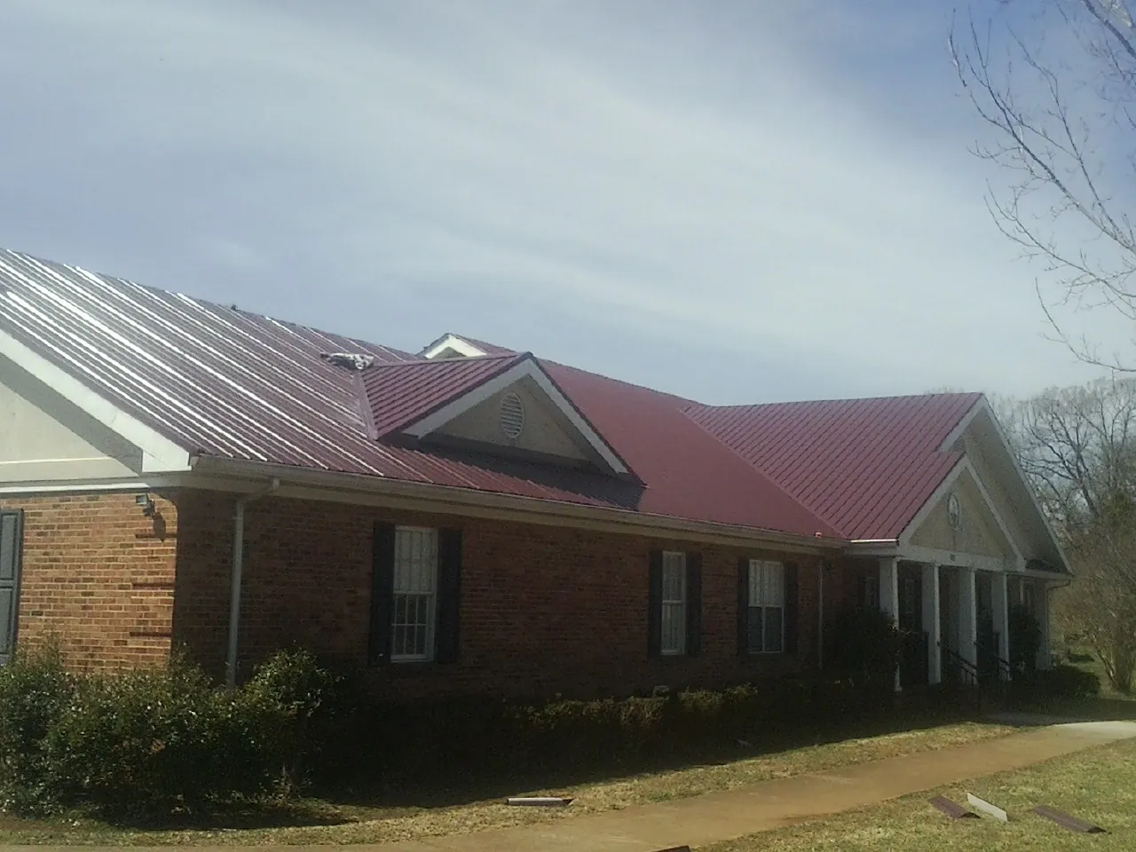 Red metal roof with gabled entries on a long brick building, from a Hail Damage Roof Repair job in Newborn