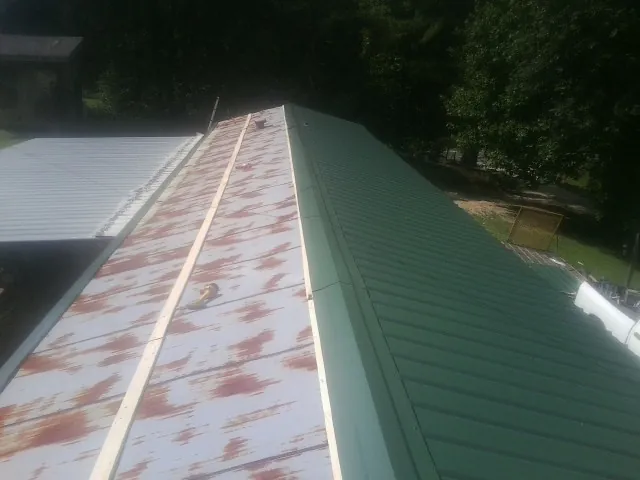 Old rusted panels beside newly installed green metal roofing — Wind Damage Roof Repair by Roofing Brothers in Newborn