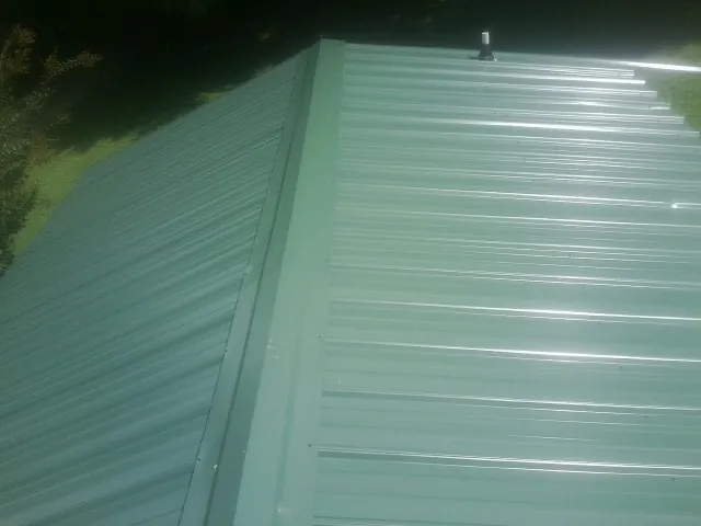 New green metal panels meeting at the ridge of a roof — Flat Roof Repair work by our crew in Newborn