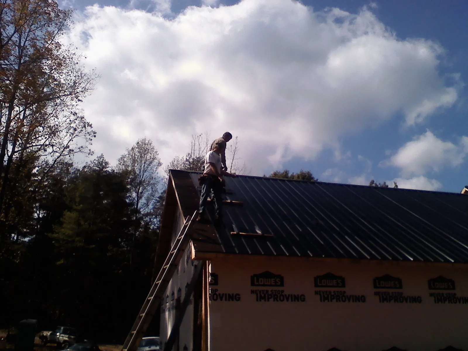 Roofer fastening dark metal panels high against a cloudy sky, from a Roof Inspection job in Newborn