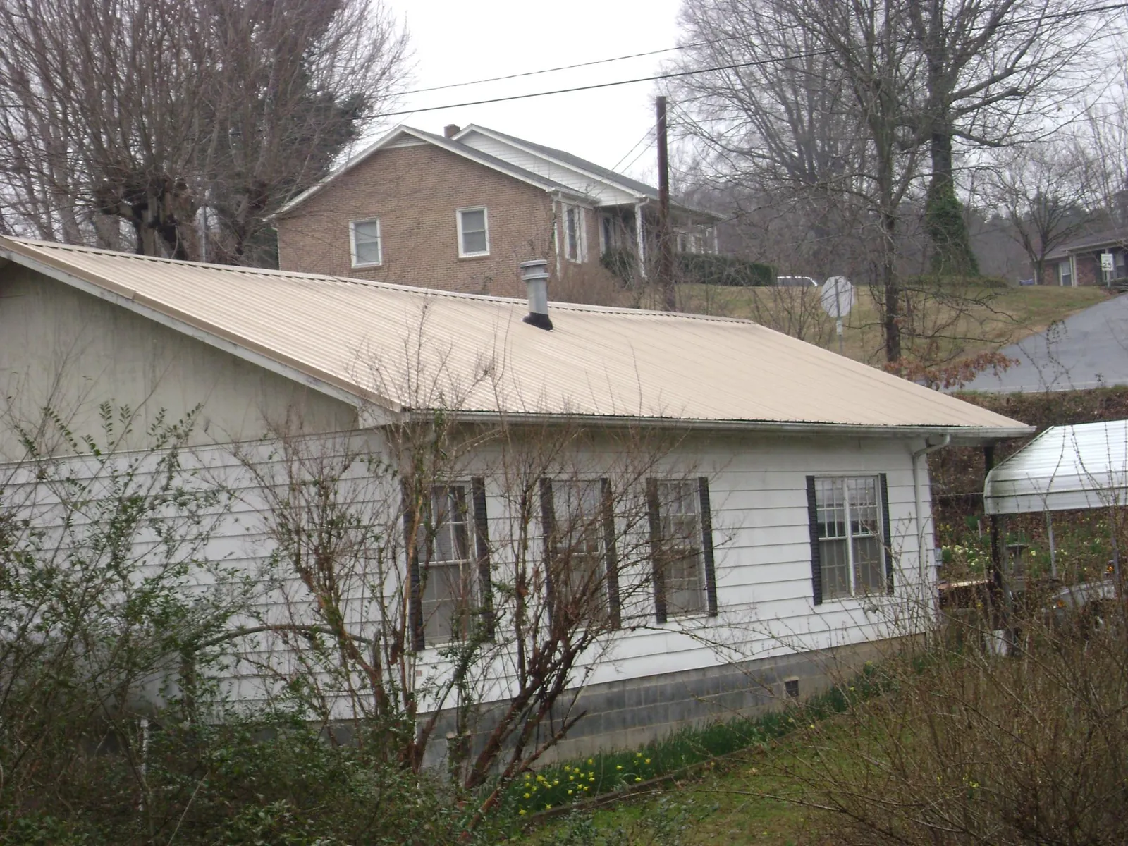 Tan metal roof on a white sided house set into a hillside — Commercial Roofing by Roofing Brothers in Newborn