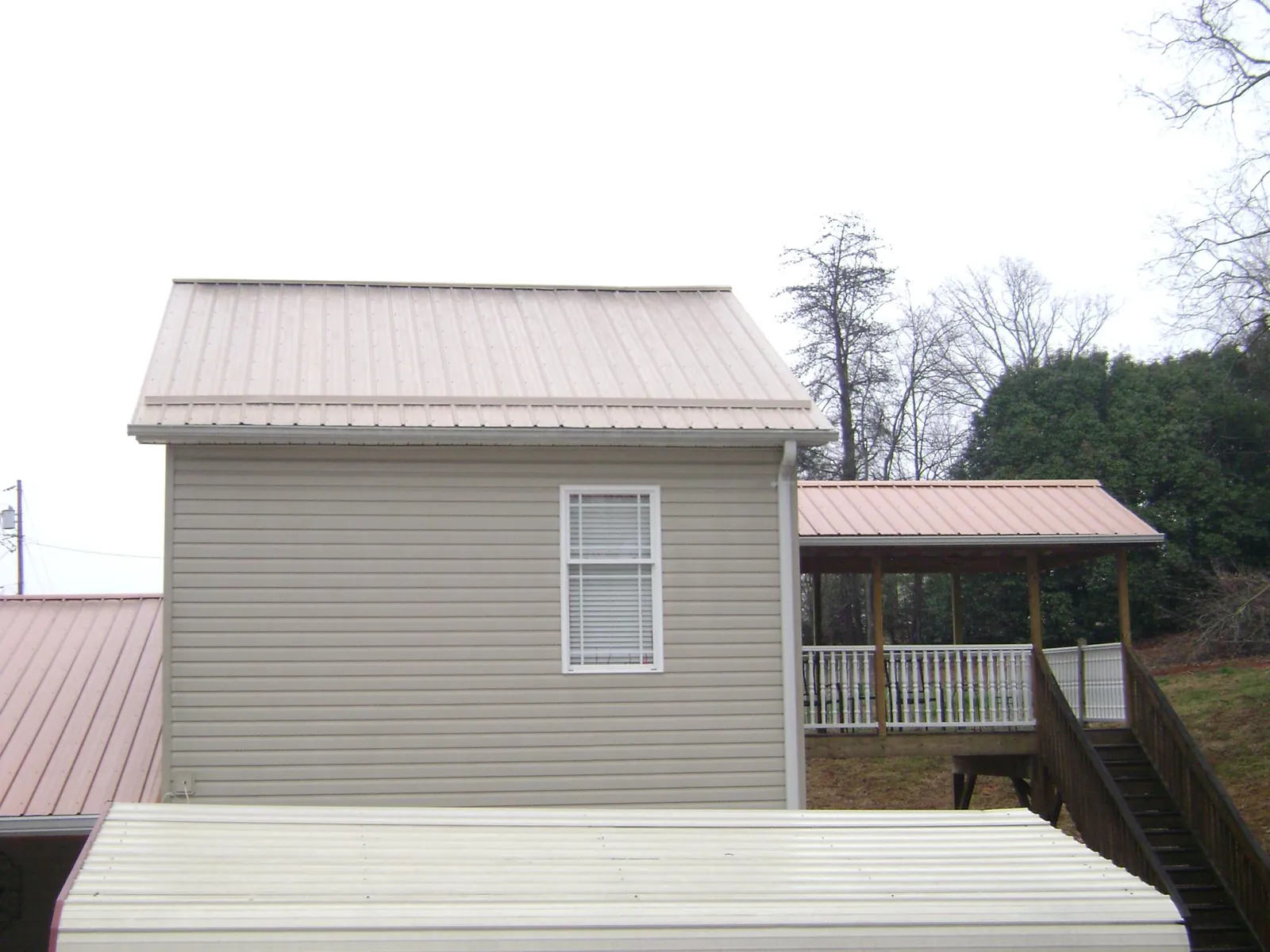Tan metal roofs on a two story addition and attached porch, from a Roof Replacement job in Newborn