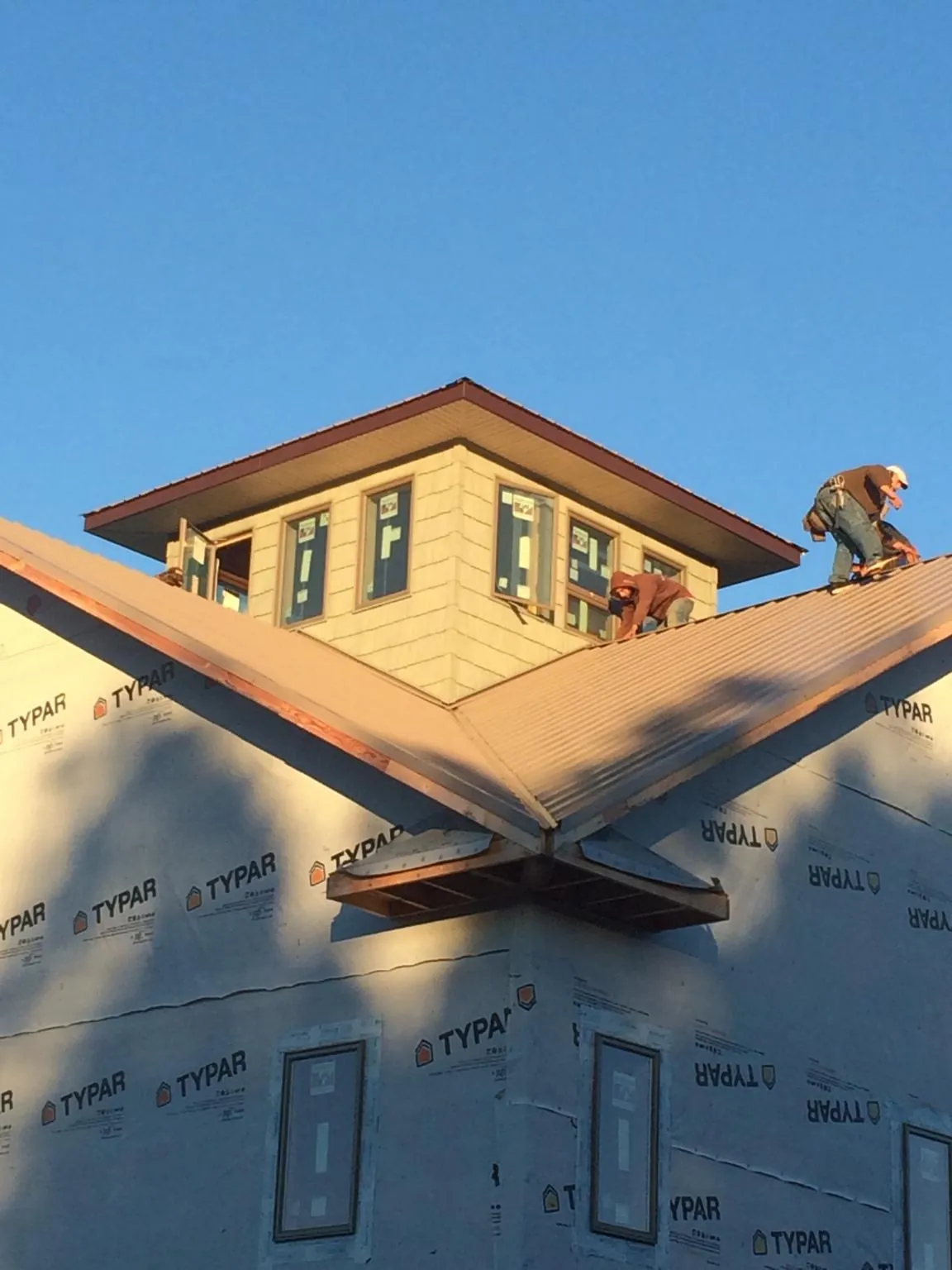 Roofers working around a rooftop cupola on a new metal roof at sunset — Roof Waterproofing in Newborn by Roofing Brothers